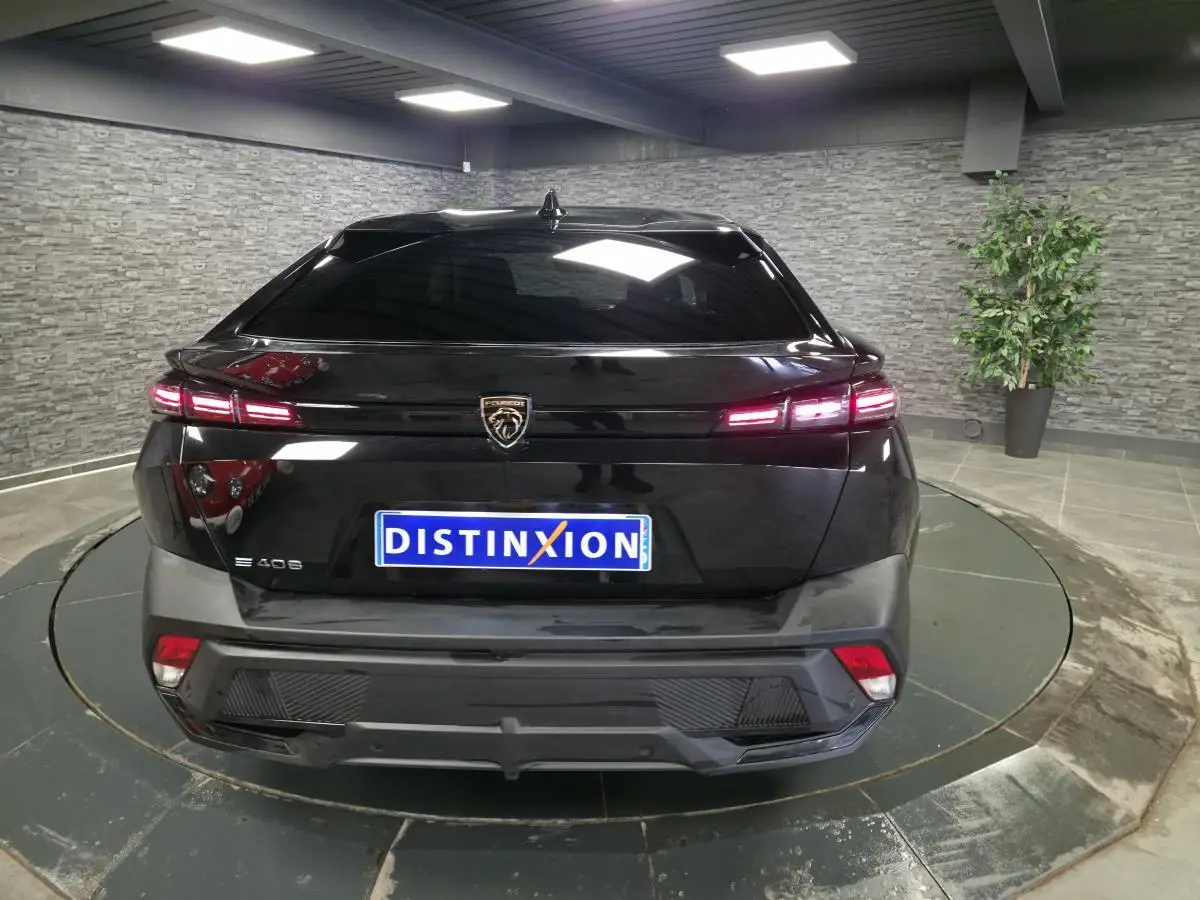 Vue arrière d'une Peugeot 408 électrique noire avec feux LED allumés dans un showroom moderne.