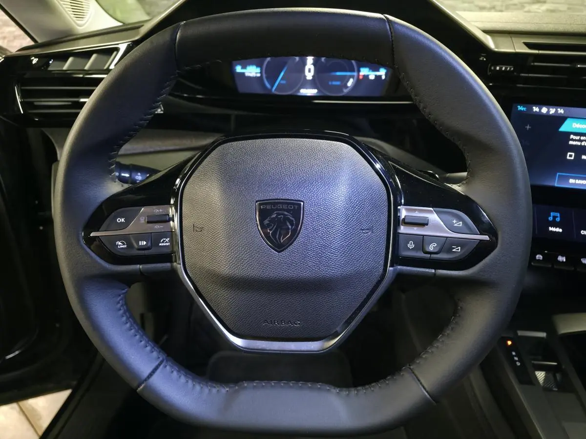 Vue rapprochée du volant cuir noir du Peugeot 408 électrique 2024 avec commandes intégrées et tableau de bord numérique.