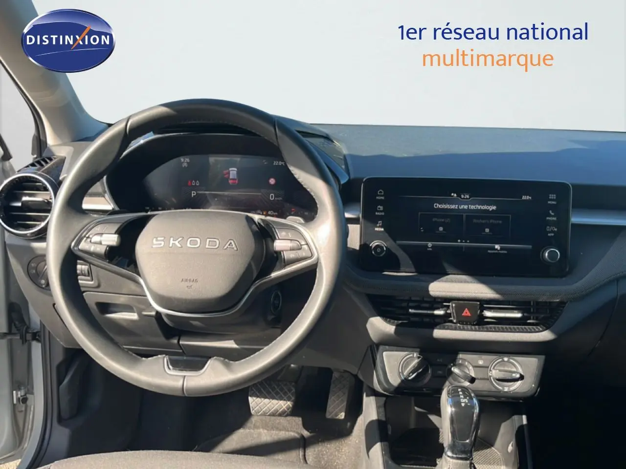 Vue intérieure centrée sur le volant SKODA et le tableau de bord avec écran tactile, ambiance gris noir moderne.