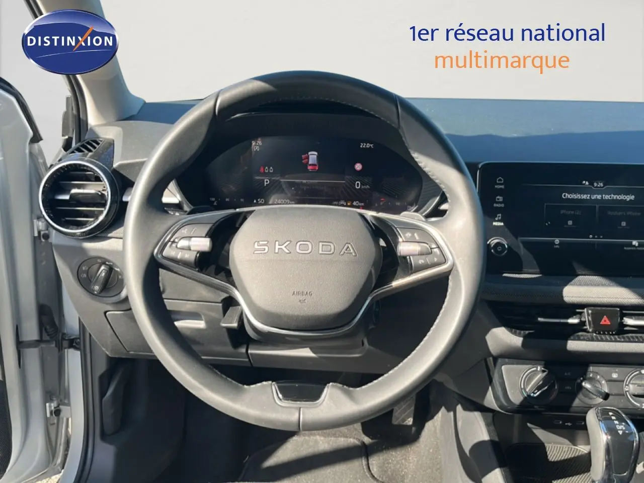 Vue intérieure centrée sur le volant SKODA d'une Fabia 2025, tableau de bord numérique et écran tactile visibles.