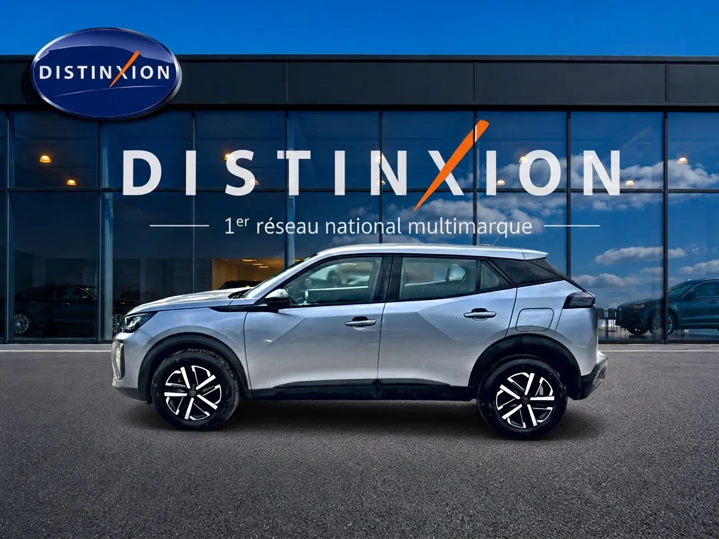 Profil côté gauche d’un Peugeot 2008 gris 2025 avec jantes noires et toit noir devant une vitrine Distinxion.