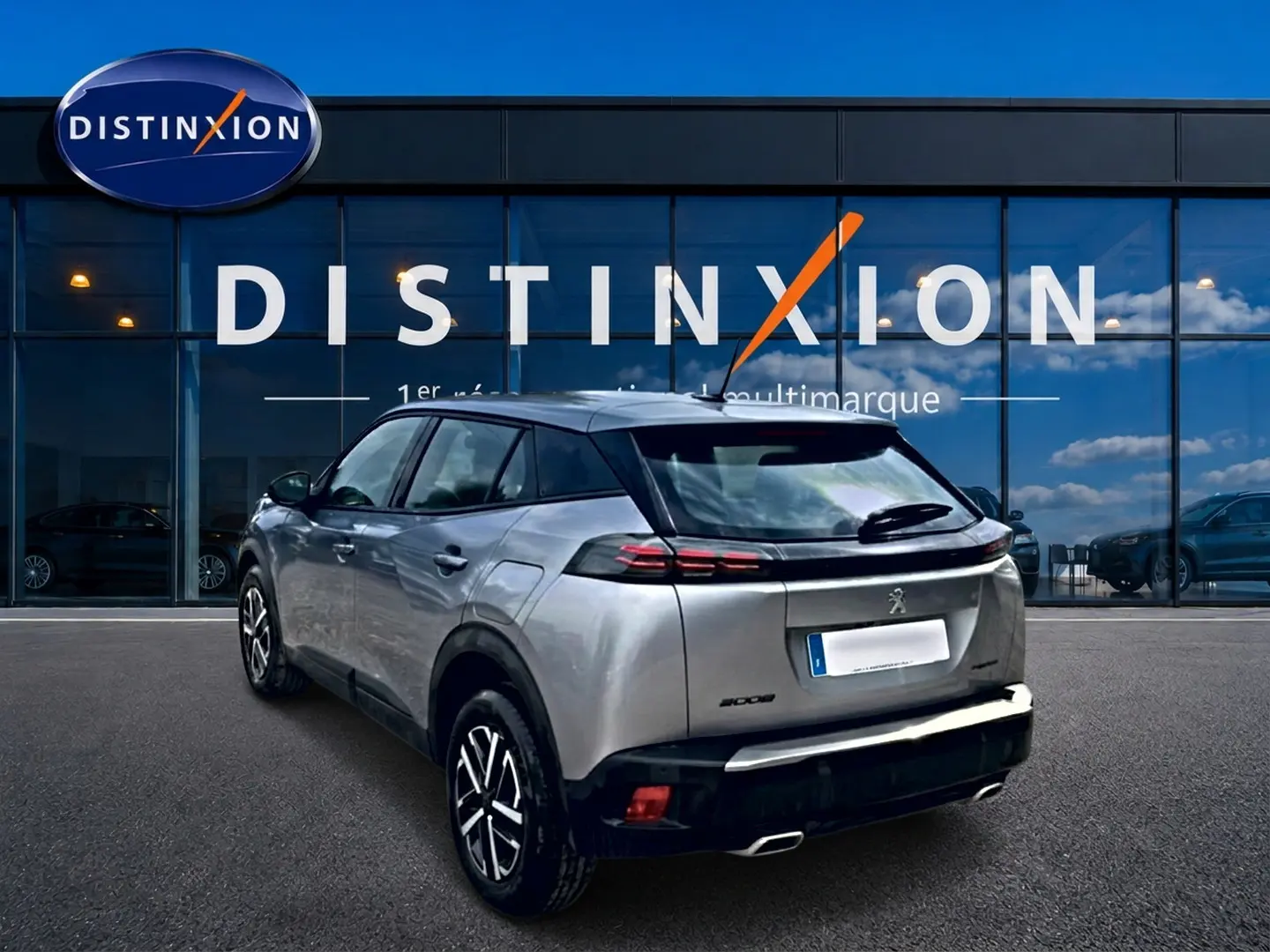 Peugeot 2008 gris en 3/4 arrière droit, avec feux arrière LED et toit noir contrastant, devant un showroom Distinxion.