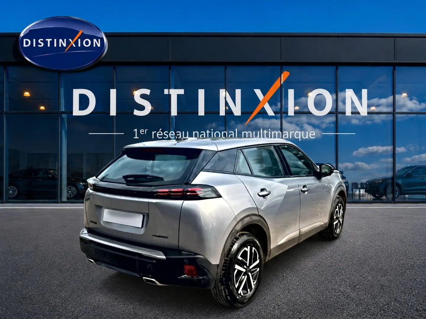 Vue 3/4 arrière droite d'un Peugeot 2008 gris 2025 avec becquet arrière et feux LED, stationné devant une vitrine Distinxion.