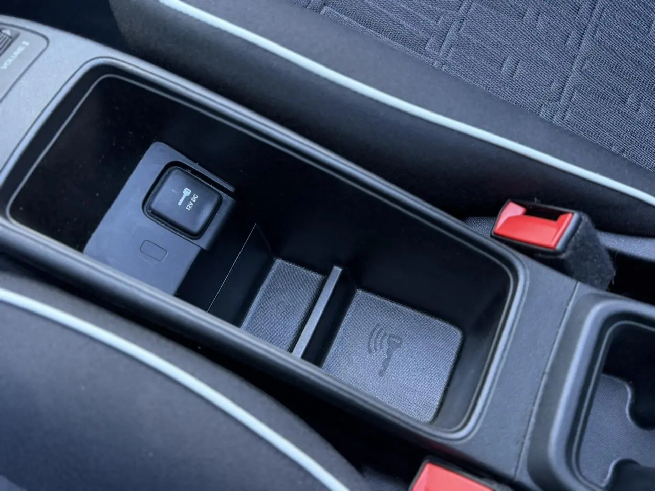 Vue rapprochée de la console centrale noire de la Fiat 500 Cabriolet électrique, montrant un port 12V et un espace de rangement.
