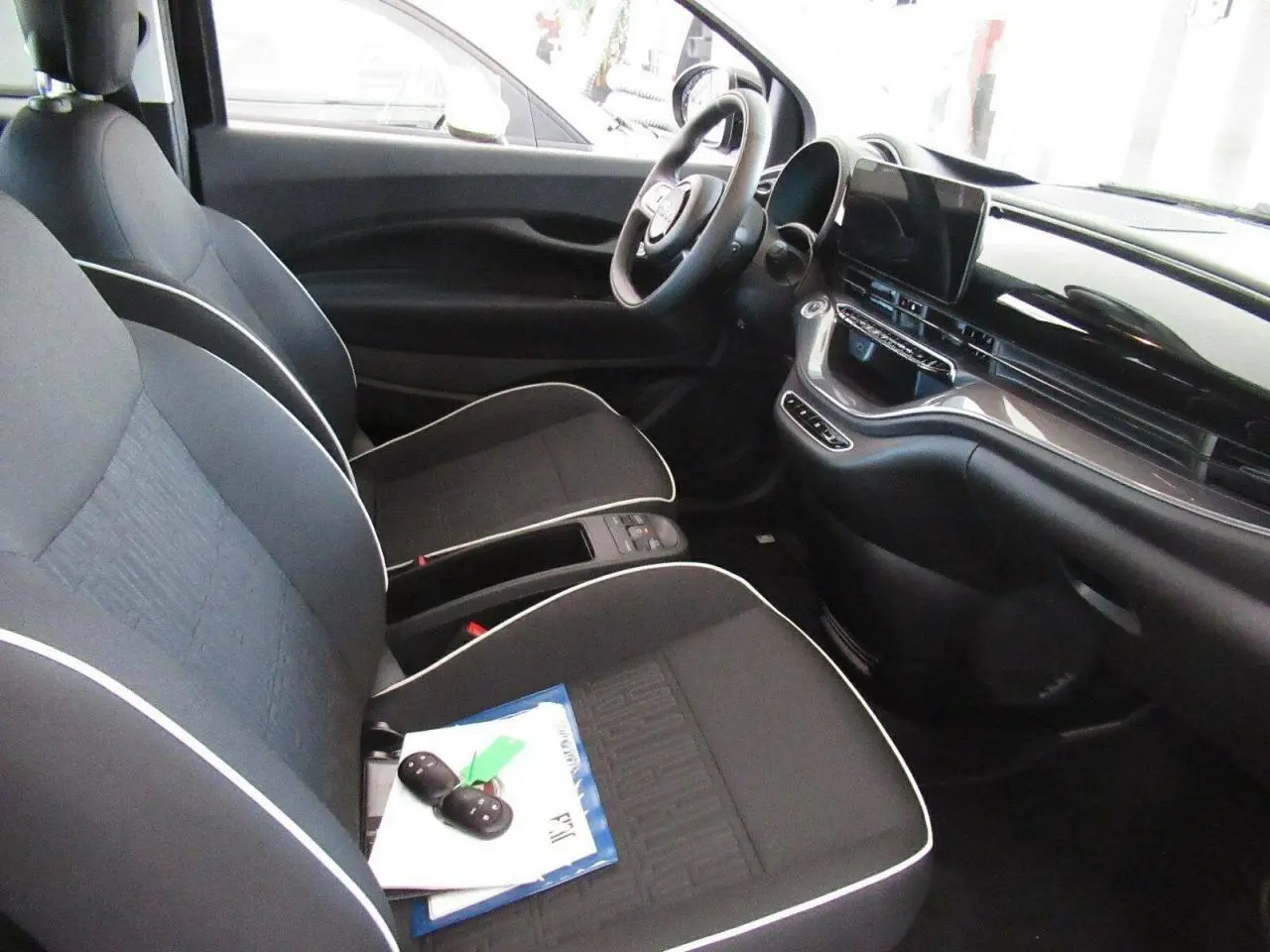 Vue intérieure avant droite de la Fiat 500 Cabriolet électrique 2024, sièges noirs avec surpiqûres blanches et tableau de bord moderne.