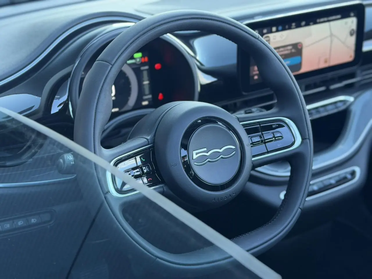 Vue rapprochée du volant noir de la Fiat 500 électrique 2024 avec tableau de bord numérique et écran tactile.
