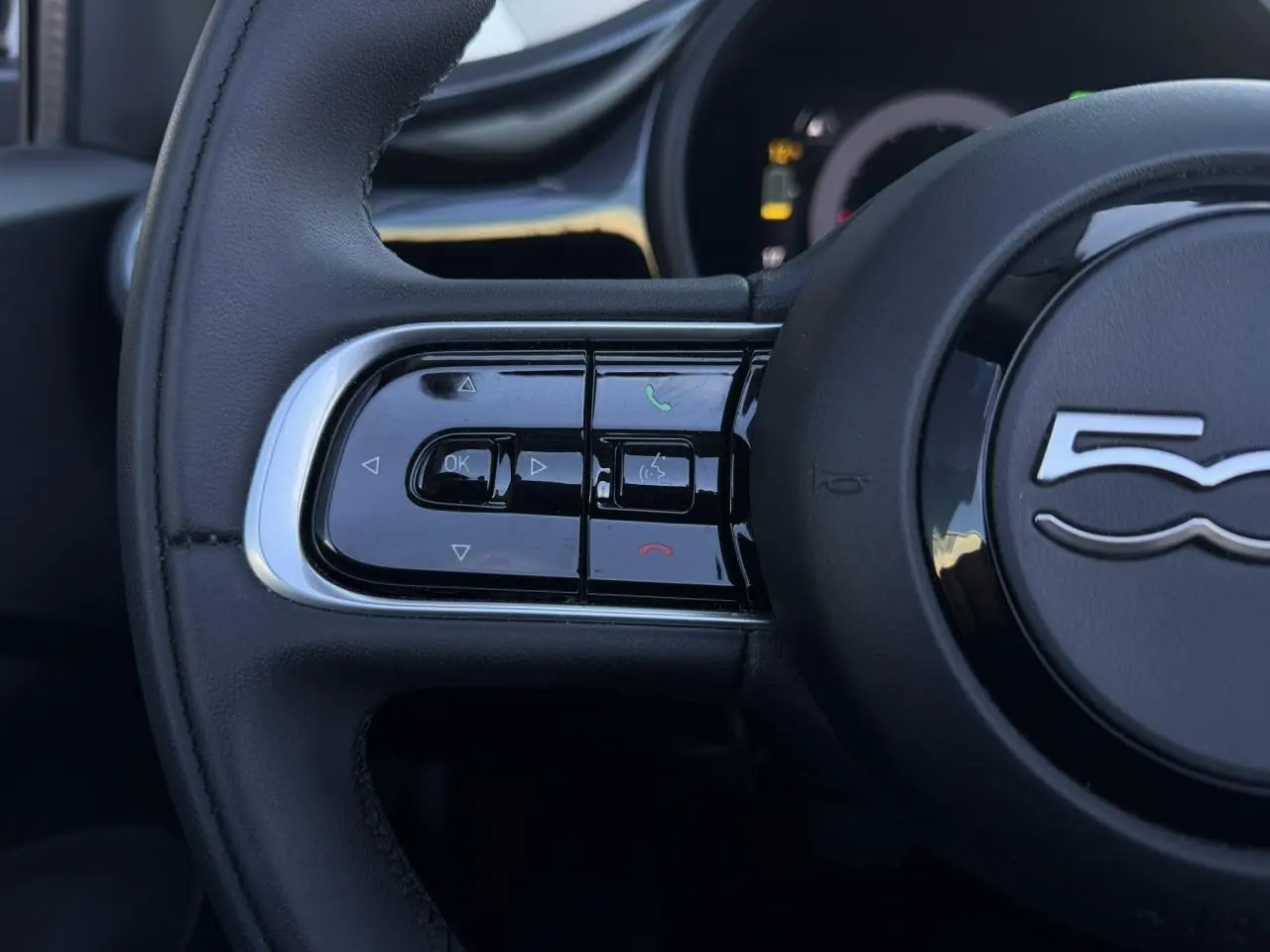 Gros plan sur les commandes gauche du volant noir de la FIAT 500 Cabriolet électrique 2024 avec logo 500 central.