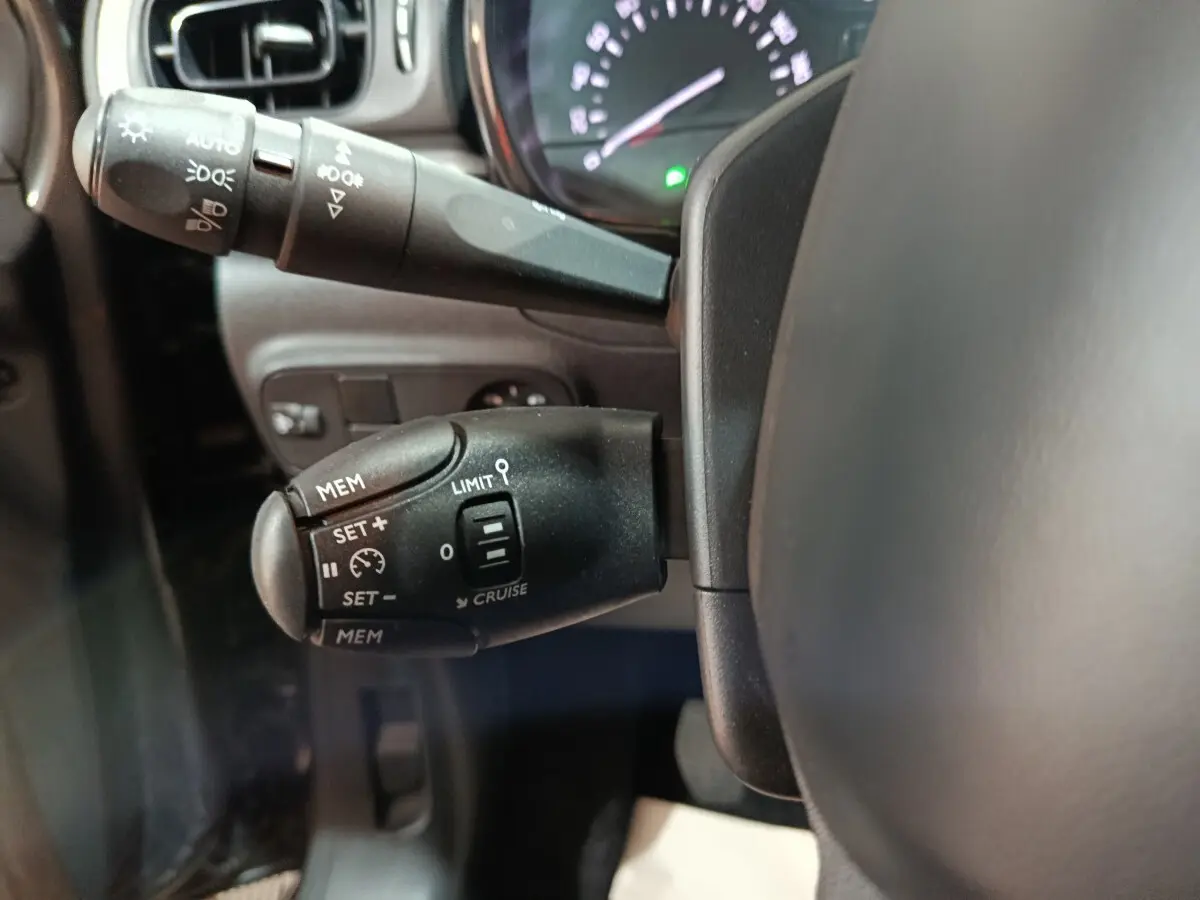 Gros plan sur la commande de régulateur de vitesse à gauche du volant d'une Citroën C3 gris foncé, tableau de bord en arrière-plan.