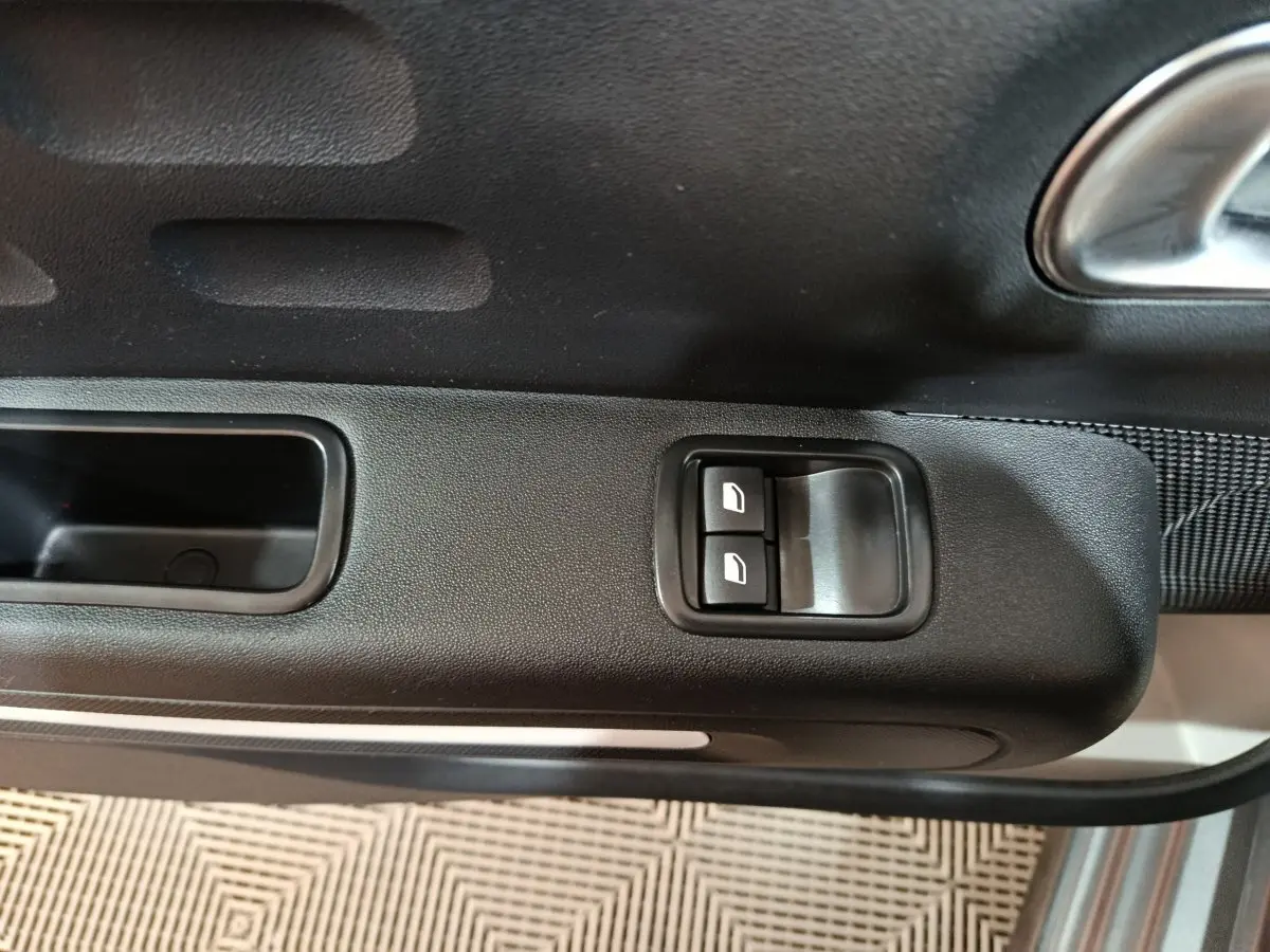 Gros plan sur les commandes des vitres électriques côté conducteur d'une Citroën C3 gris foncé, intérieur noir.