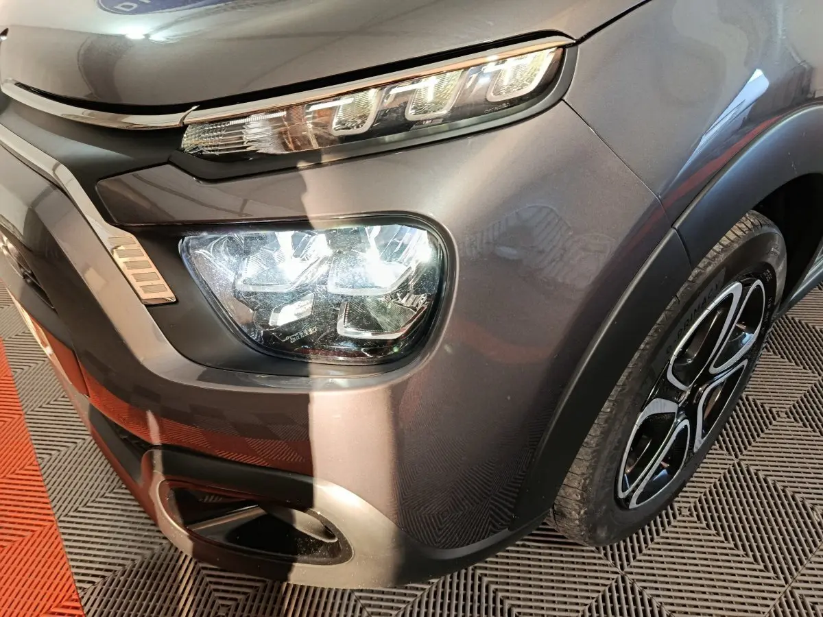 Gros plan sur l'avant droit gris foncé du Citroën C3 2024, mettant en valeur le phare LED et la jante noire à motifs.