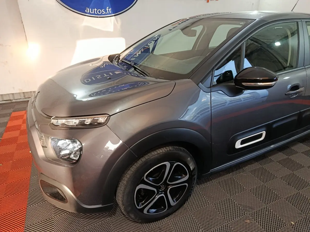 Vue 3/4 avant droit d'une Citroën C3 gris foncé avec phares LED et protections latérales noires à insert blanc.