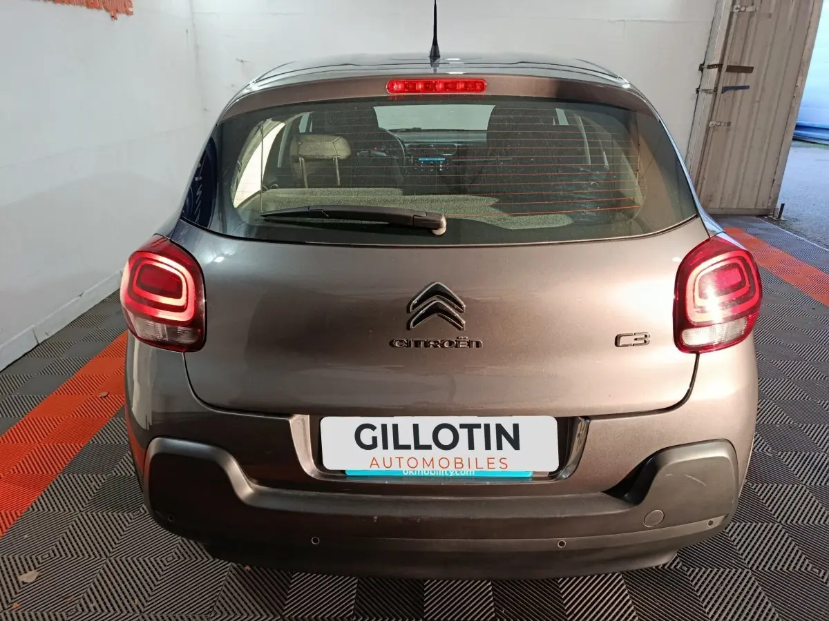 Vue arrière d'une Citroën C3 gris foncé 2024 avec feux LED allumés et logo visible sur un sol à damier noir et orange.