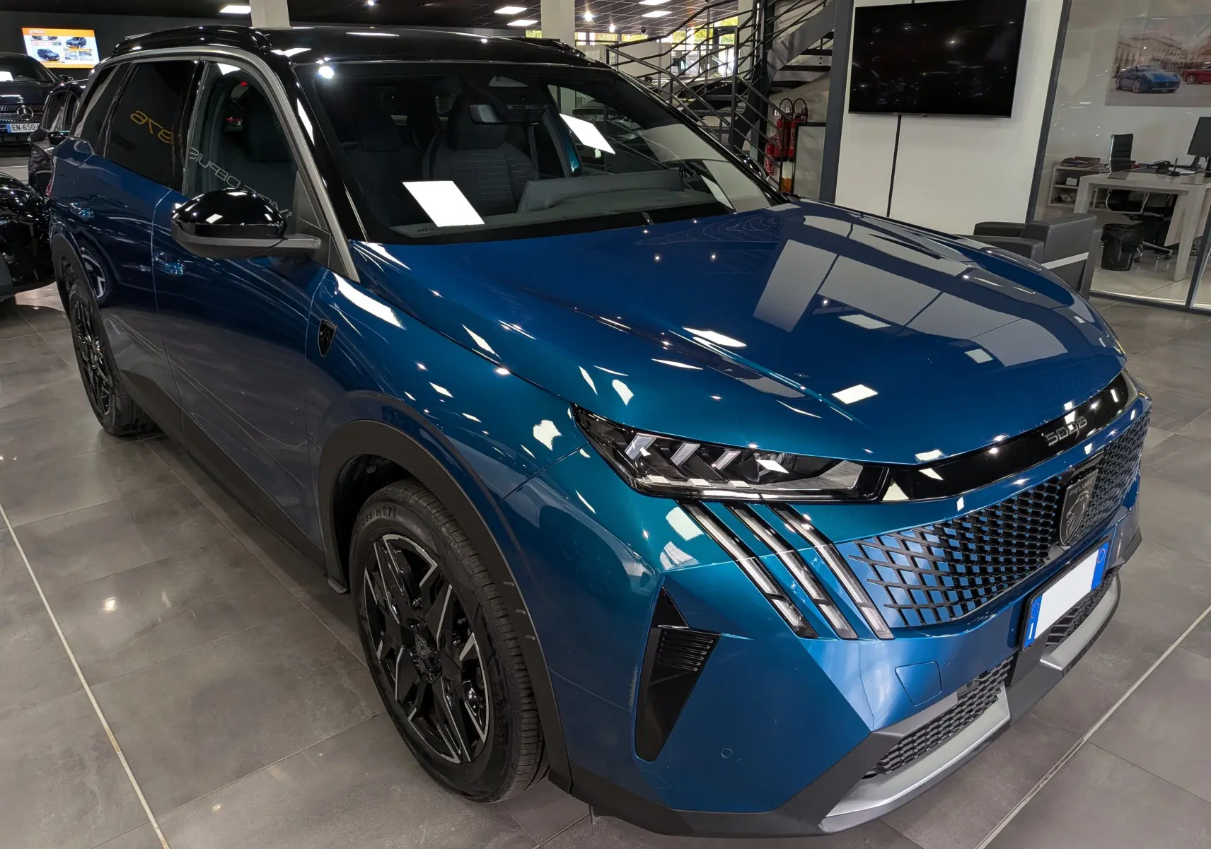 Vue 3/4 avant droit du Peugeot 5008 Hybrid bleu Obsession avec toit noir et jantes noires en concession.