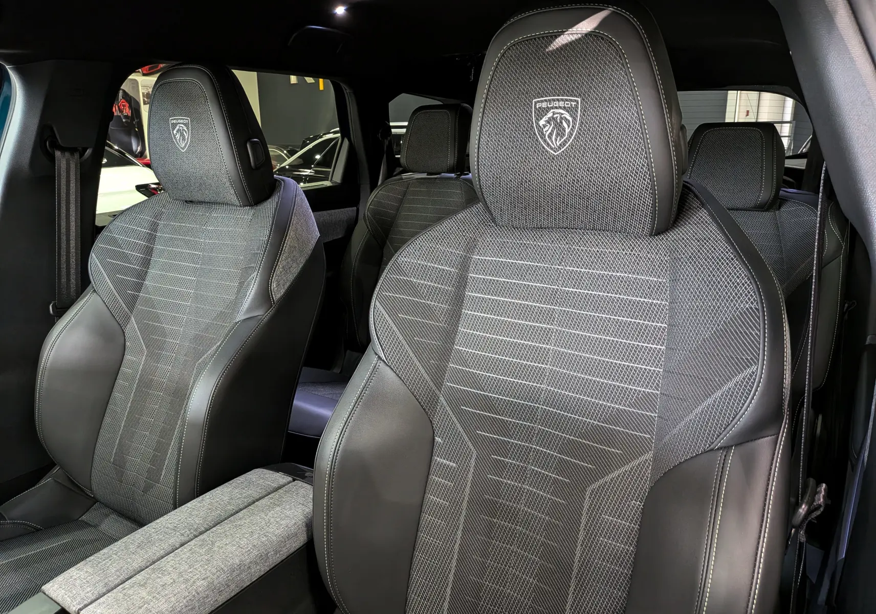 Gros plan sur les sièges avant en cuir noir et tissu gris du Peugeot 5008 Hybrid 145 CH e-DCS6 GT, intérieur raffiné.