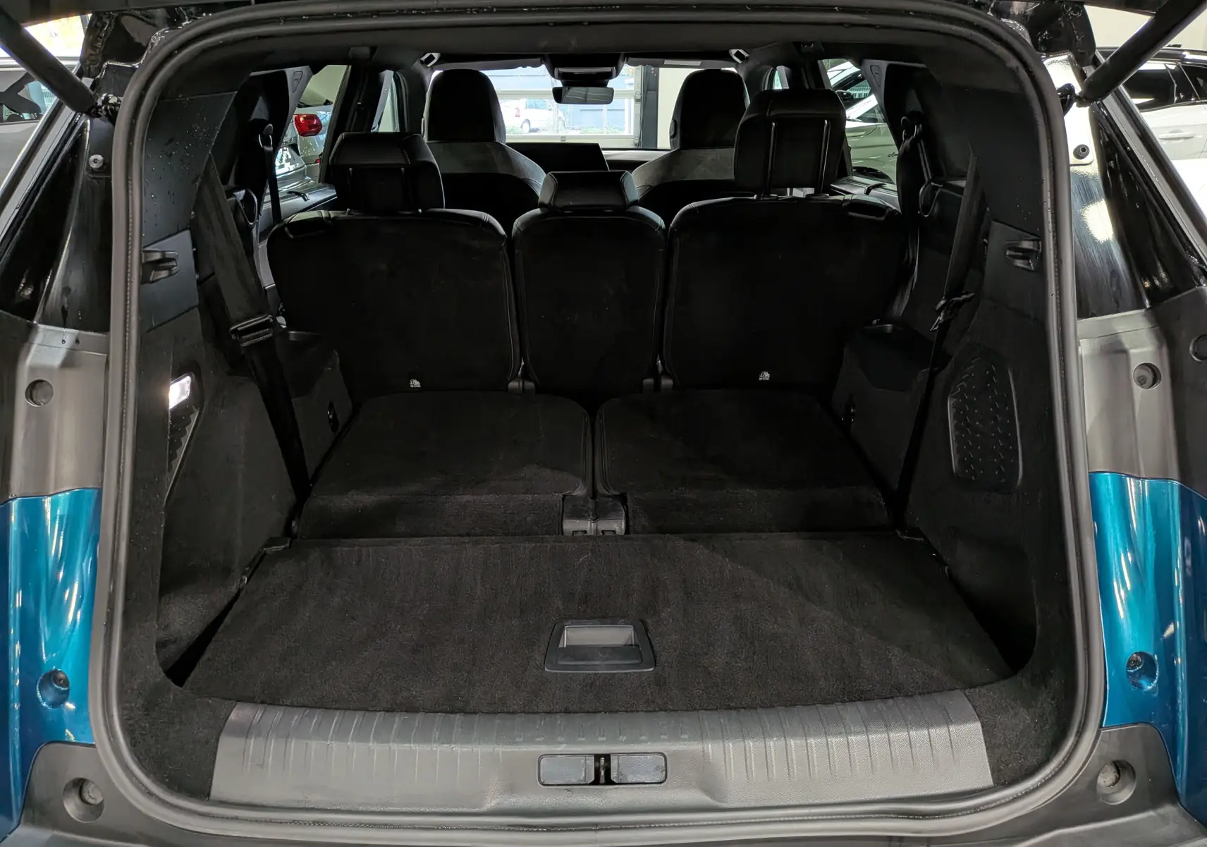 Coffre ouvert vu de l'arrière d'un Peugeot 5008 Hybrid bleu Obsession avec toit noir, sièges arrière rabattus.