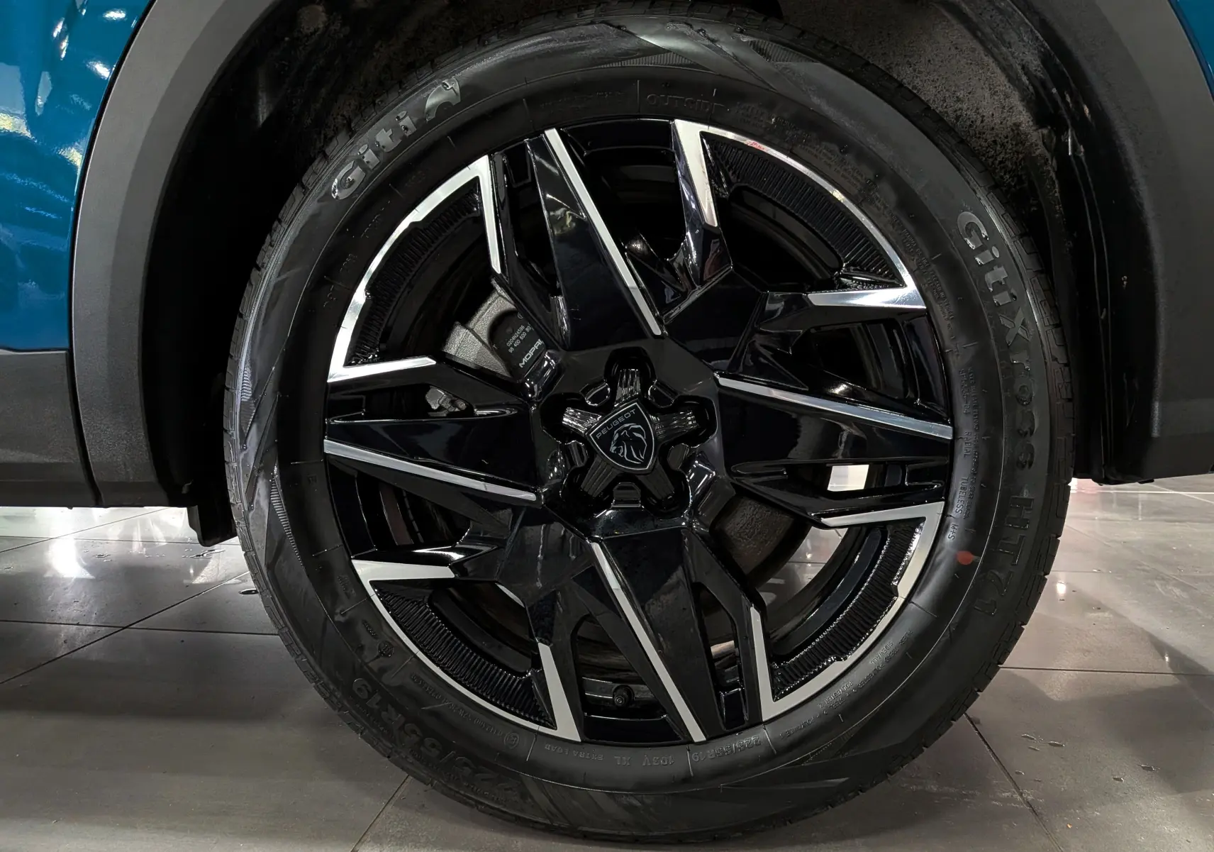 Gros plan sur la roue avant droite du Peugeot 5008 Hybrid 145 GT bleu Obsession avec jante noire et argentée.