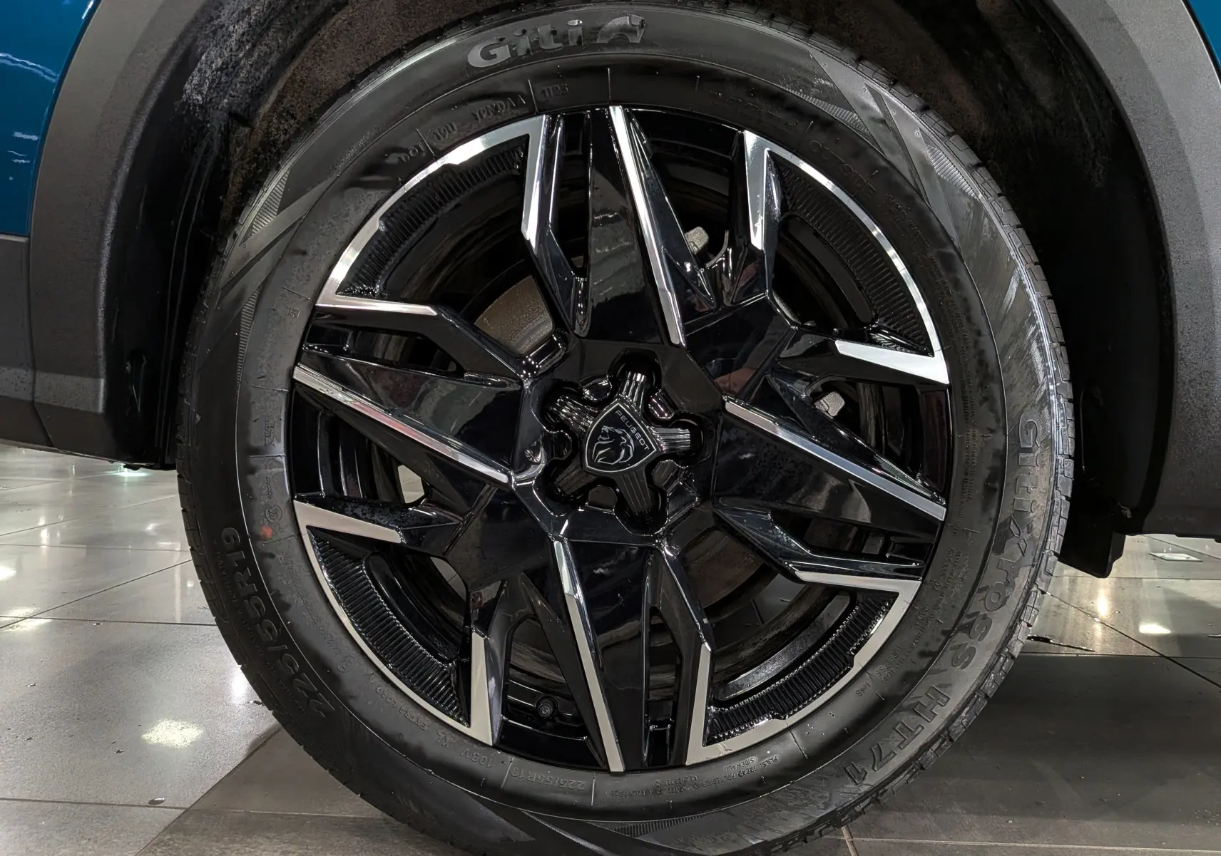 Gros plan sur la roue avant droite du Peugeot 5008 Hybrid 145 GT bleu Obsession avec jante noire et détails chromés.