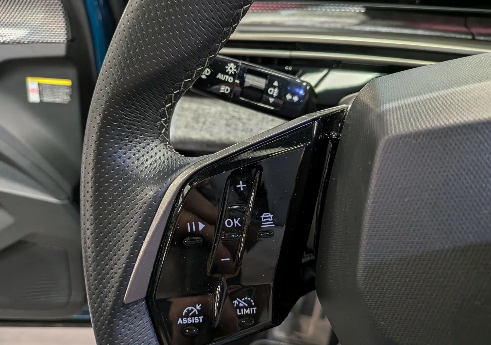 Gros plan sur les commandes au volant en cuir perforé noir du Peugeot 5008 Hybrid 145 CH e-DCS6 GT 2025.