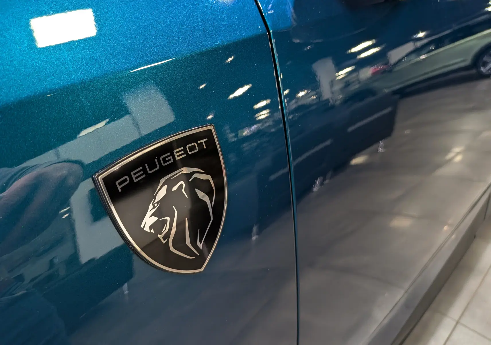 Gros plan sur l’écusson Peugeot noir et argent sur la porte côté gauche d’un 5008 bleu Obsession.