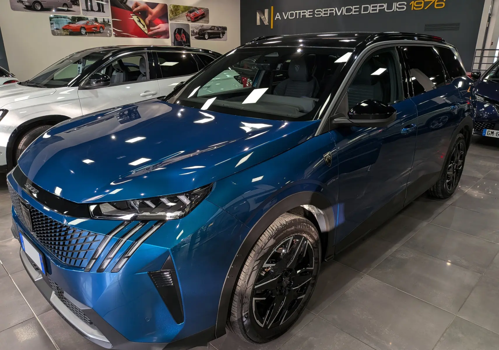 Vue 3/4 avant droite d’un Peugeot 5008 Hybrid 145 CH e-DCS6 GT bleu Obsession avec toit noir et jantes noires en showroom.