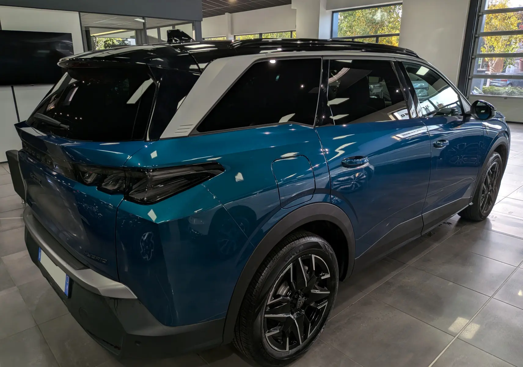 Vue 3/4 arrière droit du Peugeot 5008 Hybrid 145 GT bleu Obsession avec toit noir et jantes noires en showroom.