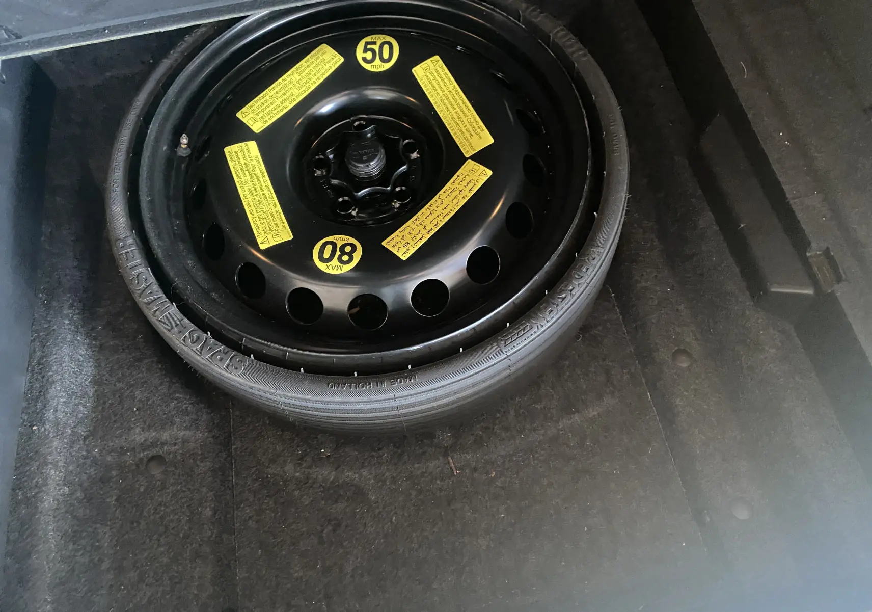 Roue de secours noire avec étiquettes jaunes dans le coffre d'un Audi Q5 blanc diesel de 2012.