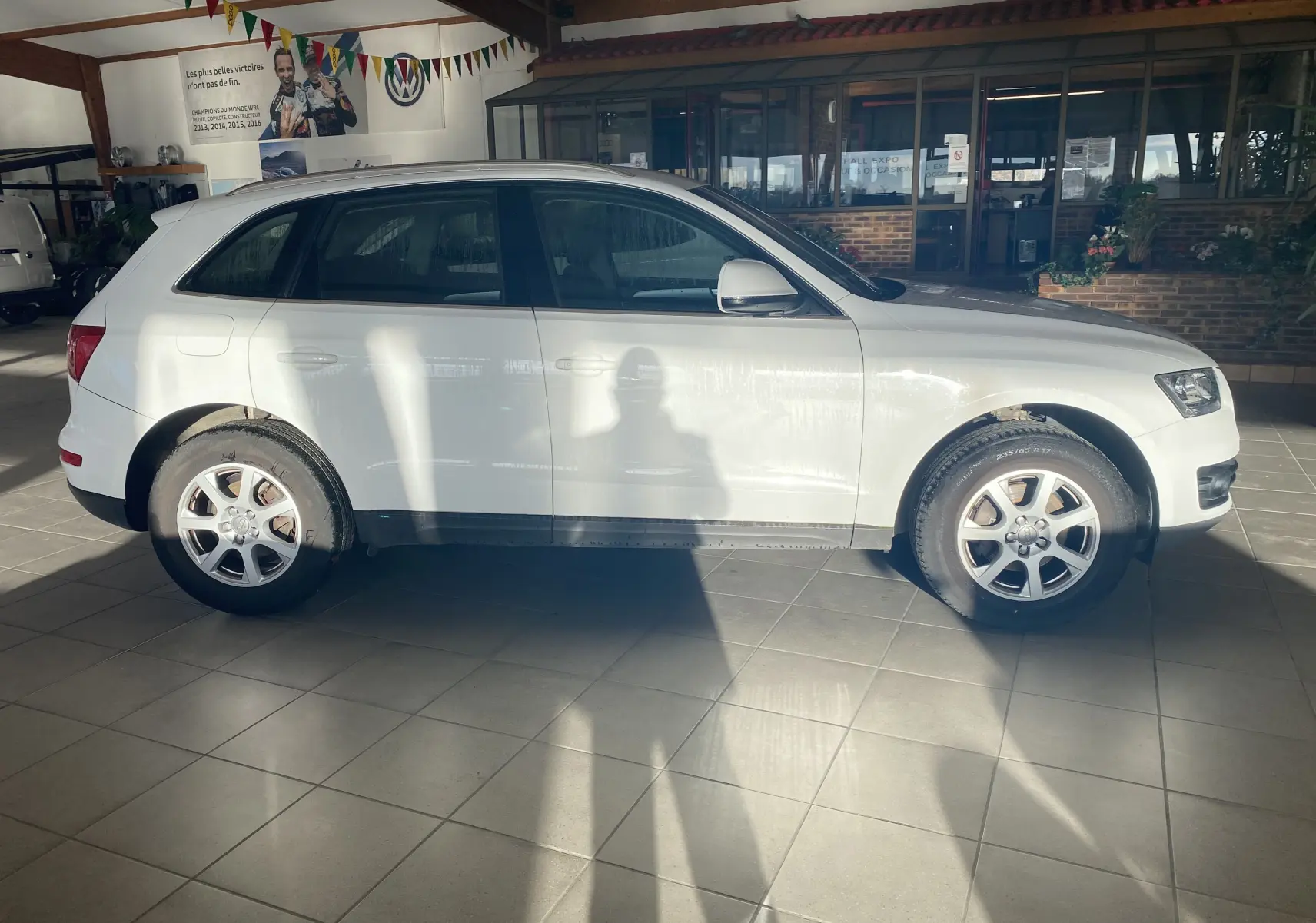 Audi Q5 blanc vue de profil côté gauche, stationné en intérieur avec jantes alliage et pneus visibles.