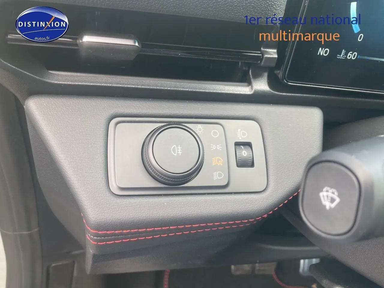 Détail du tableau de bord avec commande des phares et surpiqûres rouges dans une Ford Puma gris cactus 2025.