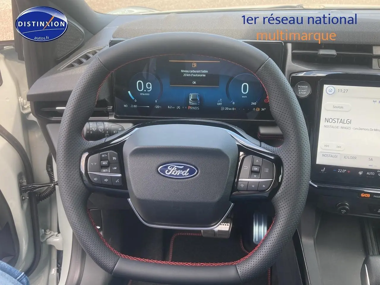 Vue rapprochée du volant perforé avec surpiqûres rouges du Ford Puma gris cactus 2025, tableau de bord numérique visible.