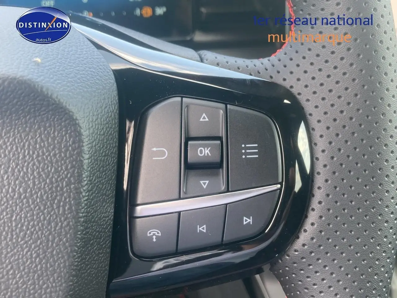 Gros plan sur les commandes multifonctions noires du volant perforé du Ford Puma gris cactus 2025.