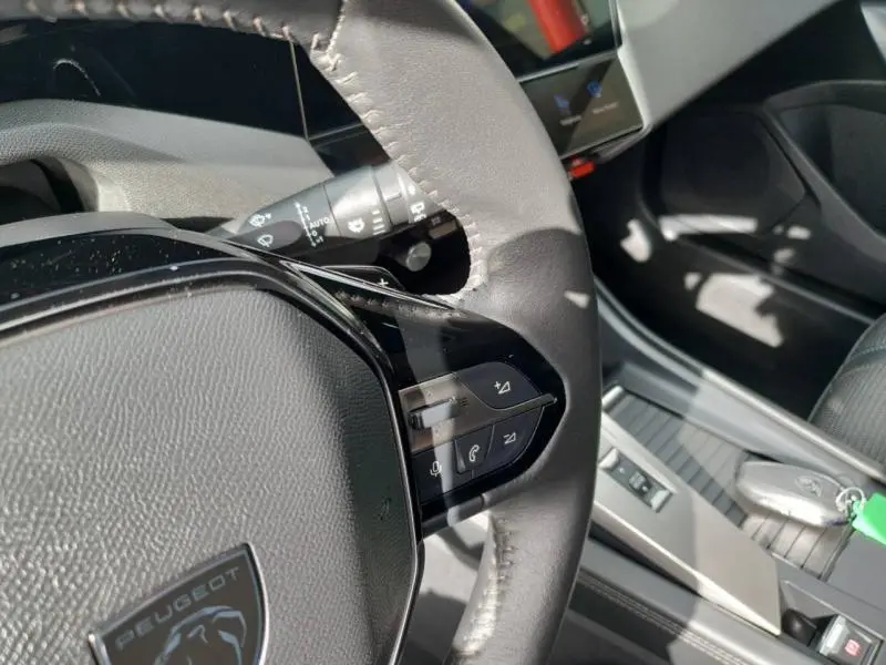 Gros plan sur le volant multifonction de la Peugeot 308 2024 avec commandes audio et téléphone, intérieur gris.