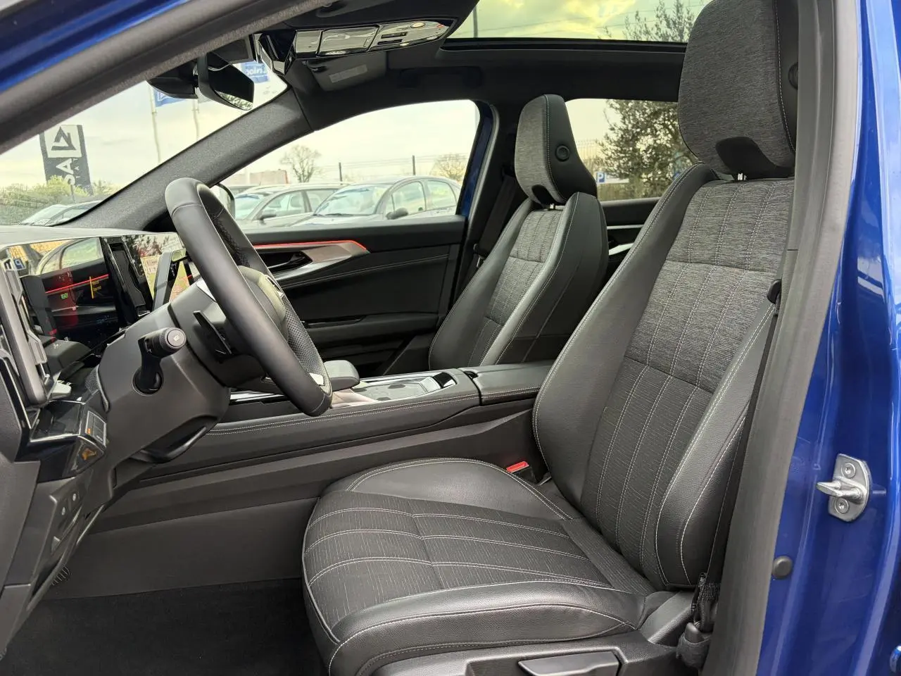 Vue intérieure côté conducteur du Renault Austral bleu, montrant les sièges gris et le volant textile enduit.