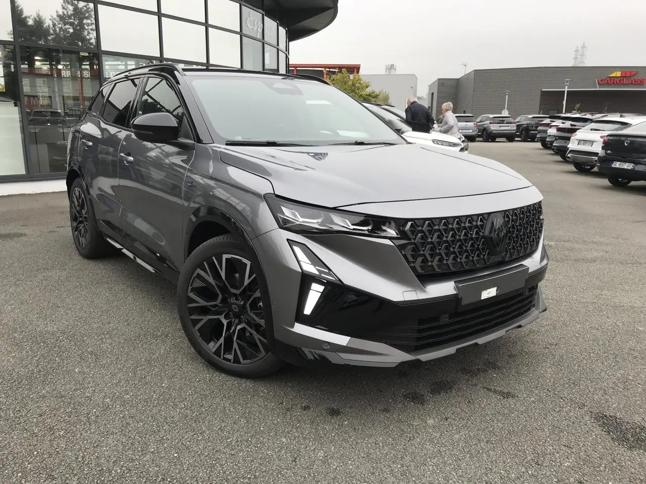 Renault Austral full hybrid gris et noir, vue 3/4 avant avec calandre noire et jantes alliage 20 pouces.