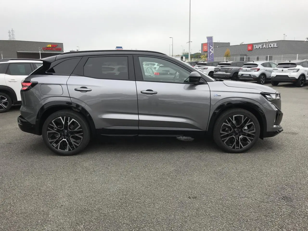 Profil droit du Renault Austral gris métallisé avec toit noir, jantes alliage noires et détails Esprit Alpine visibles.