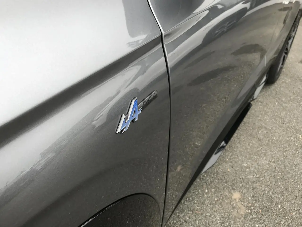 Gros plan sur l'aile avant gauche gris métallisé du Renault Austral avec logo Esprit Alpine bleu et noir.