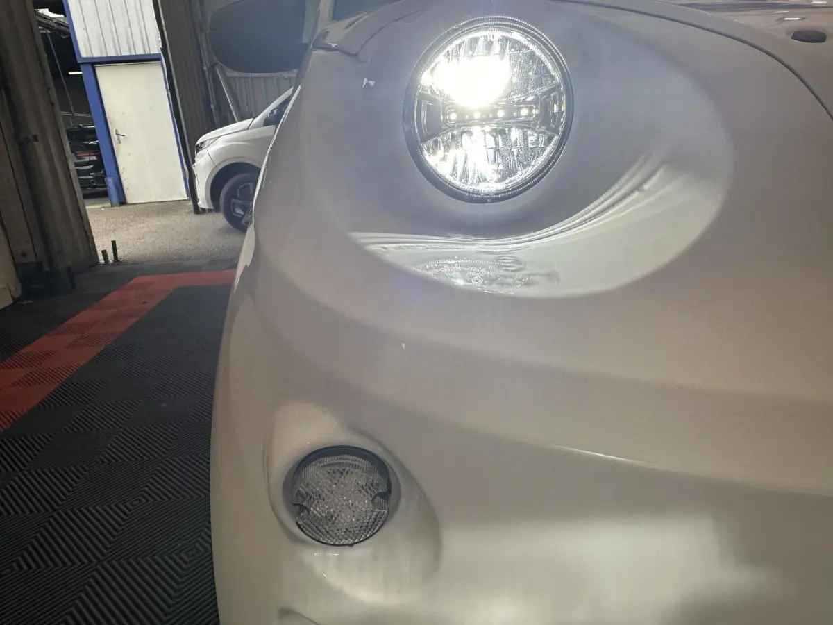 Gros plan sur le phare avant droit allumé de l'AIXAM MINAUTO E ACCESS blanc 2026, avec feu antibrouillard visible.