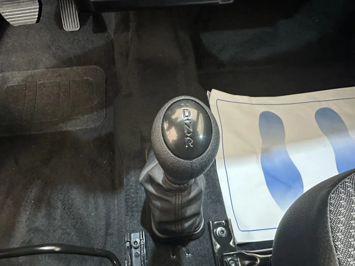 Gros plan sur le levier de vitesses automatique noir de l'AIXAM MINAUTO E ACCESS 2026, intérieur avec tapis et pédales visibles.