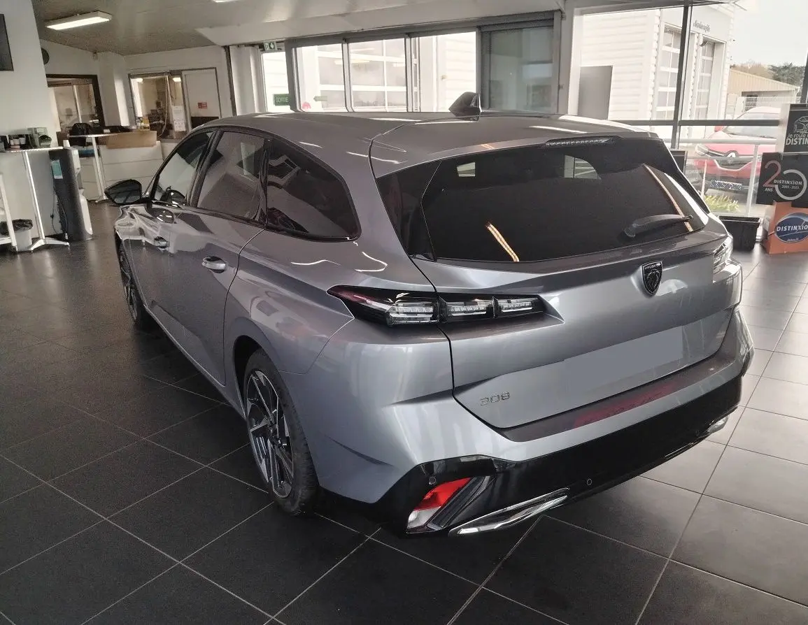 Vue 3/4 arrière droit d'une Peugeot 308 SW Hybrid gris Artense en showroom, avec feux arrière LED et jantes biton.