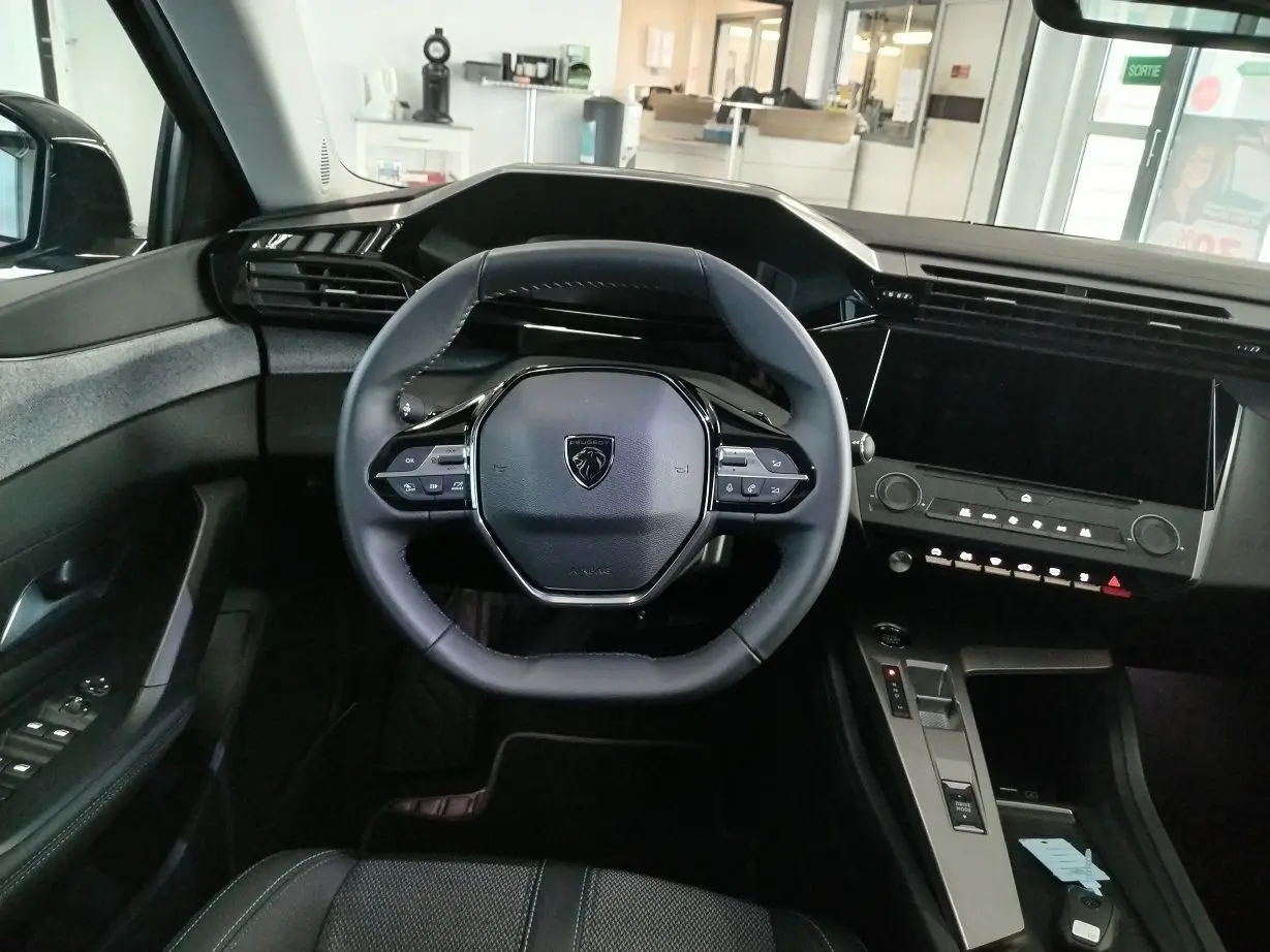 Vue intérieure frontale du poste de conduite de la Peugeot 308 SW Hybrid 145, avec volant compact et écran tactile noir.