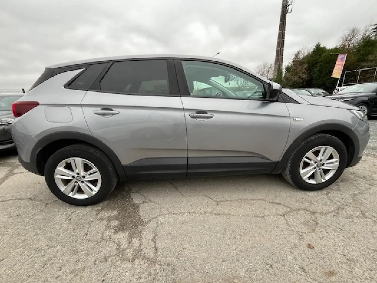 Vue de profil côté gauche d'un Opel Grandland X gris 2020 avec jantes alliage et lignes noires sur les bas de caisse.