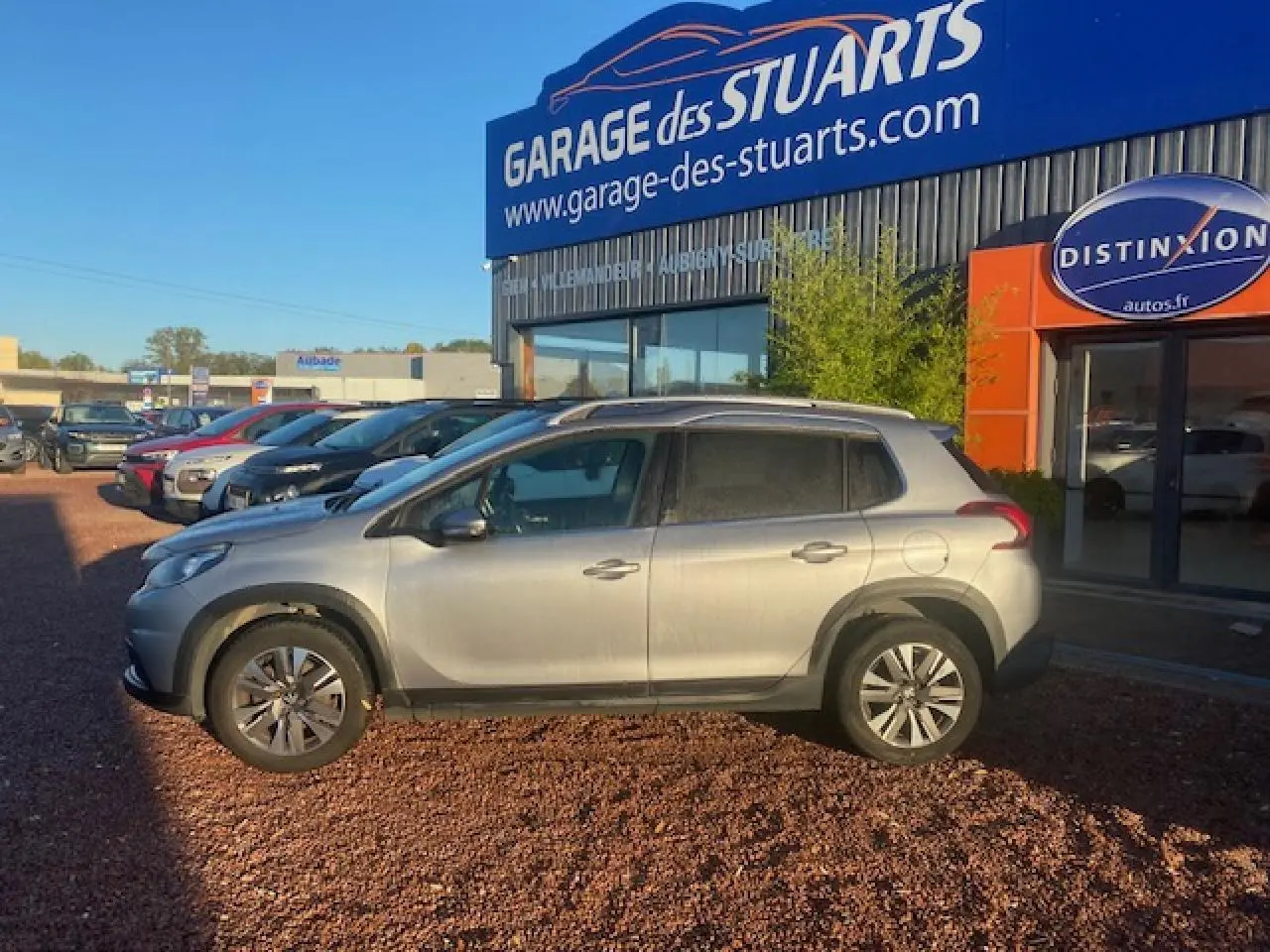 Peugeot 2008 gris Artense vue de profil côté gauche, stationnée devant un garage avec jantes aluminium 16 pouces.