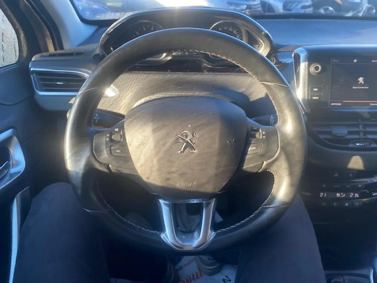 Vue intérieure centrée sur le volant cuir de la Peugeot 2008, avec écran tactile multifonction et tableau de bord visible.