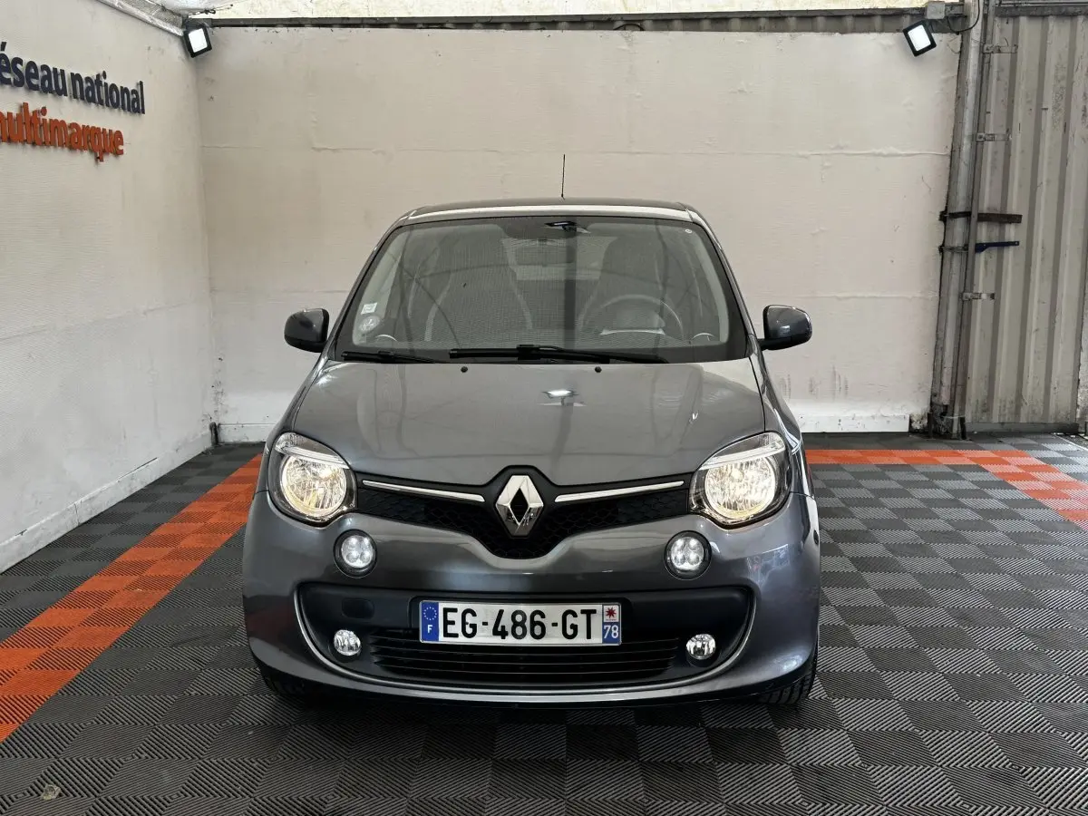 Vue de face d'une Renault Twingo Intense Energy TCe 90 gris foncé avec phares allumés dans un garage.