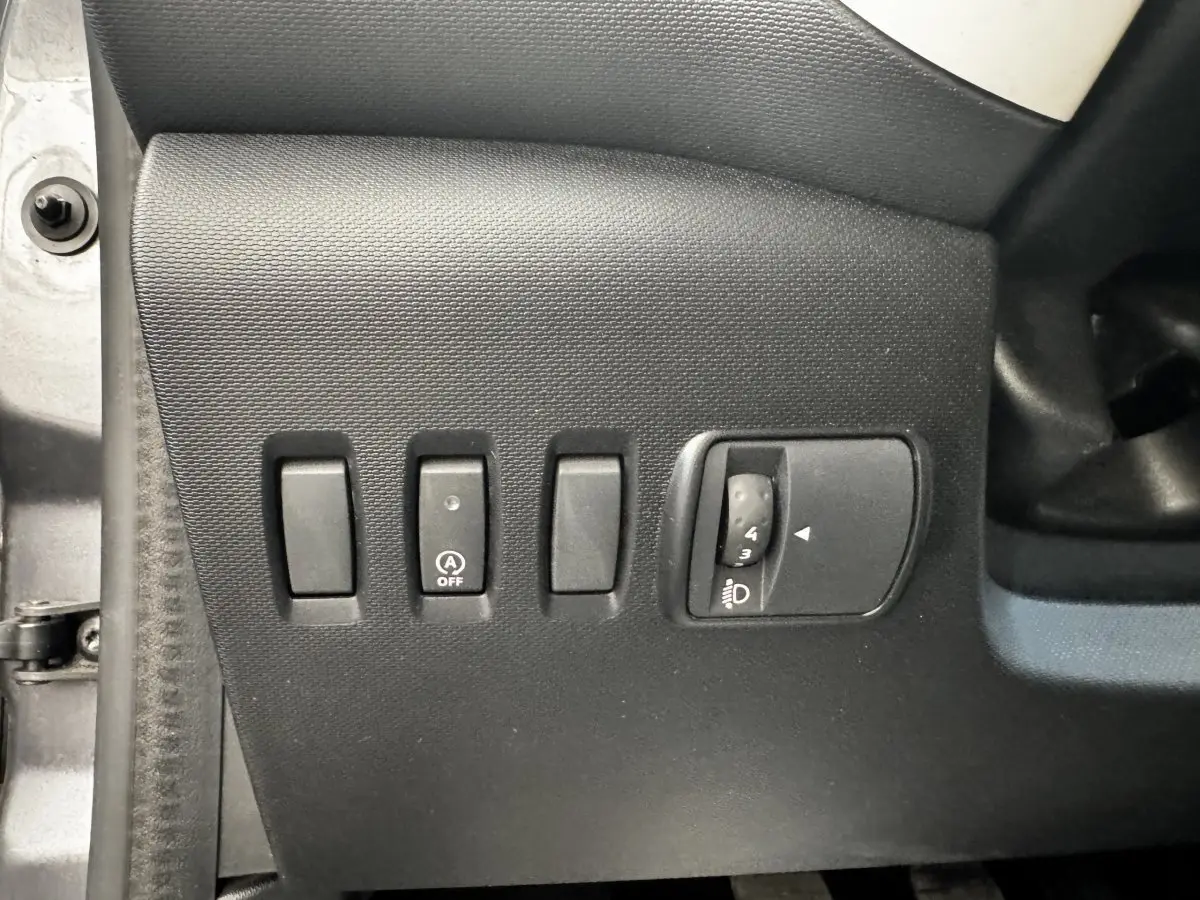 Gros plan sur les commandes de réglage des phares et désactivation du démarrage automatique, intérieur Renault Twingo gris foncé.