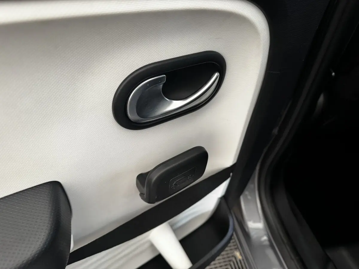 Poignée de porte intérieure côté droit de Renault Twingo gris foncé, avec ouverture de coffre manuelle visible.