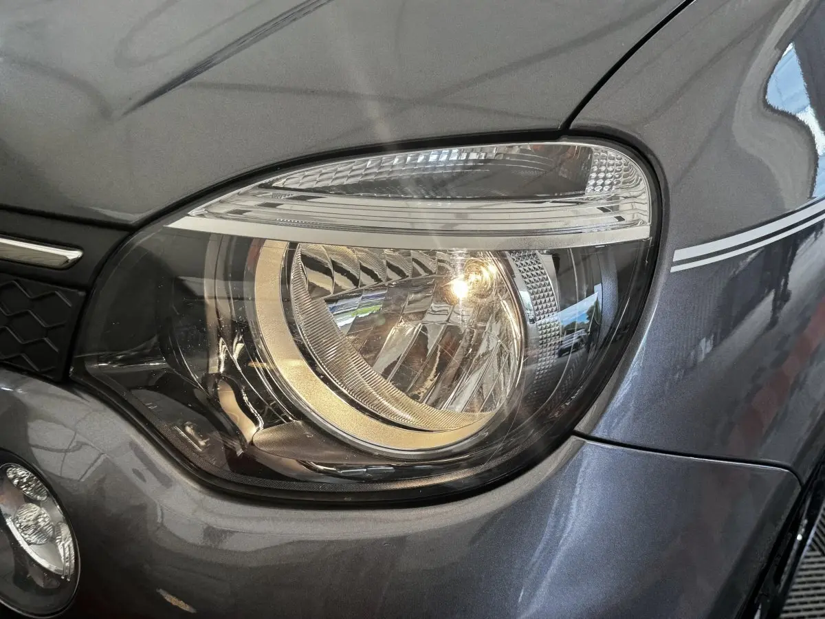 Gros plan sur le phare avant droit d'une Renault Twingo Intense Energy TCe 90 gris foncé avec bande décorative blanche.