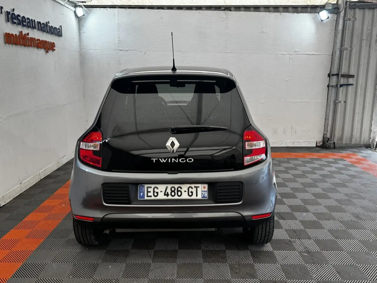 Vue arrière d'une Renault Twingo gris foncé avec vitre arrière noire et feux arrière rouges dans un garage.