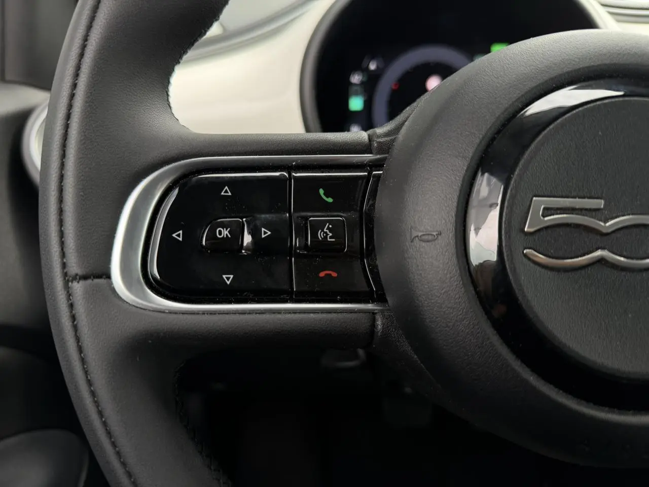 Gros plan sur le volant noir du Fiat 500 électrique 2024, avec commandes intégrées et logo 500 au centre.