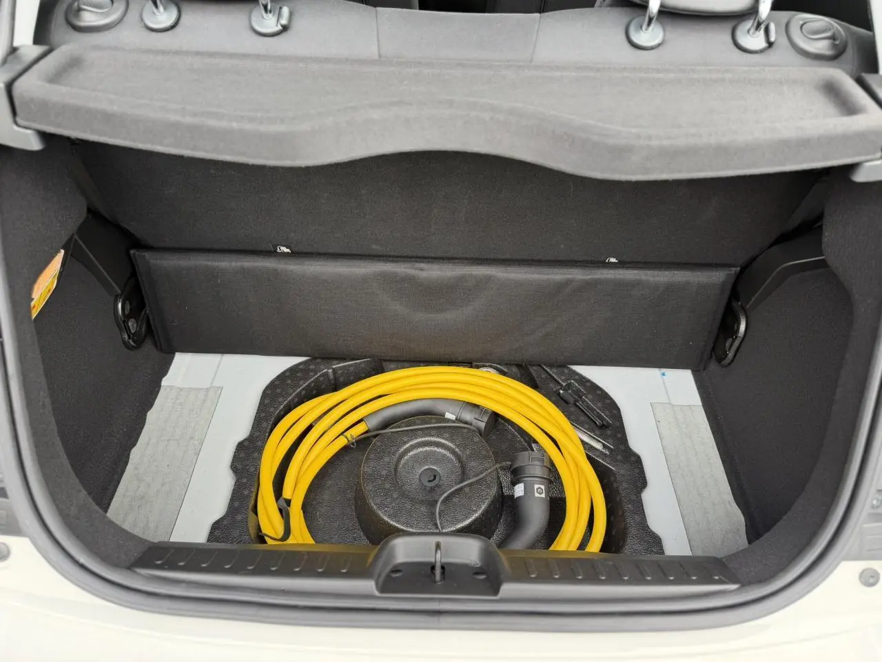 Coffre ouvert d'une FIAT 500 électrique blanc Artic, montrant le câble de recharge jaune rangé dans l'espace sous la tablette arrière.