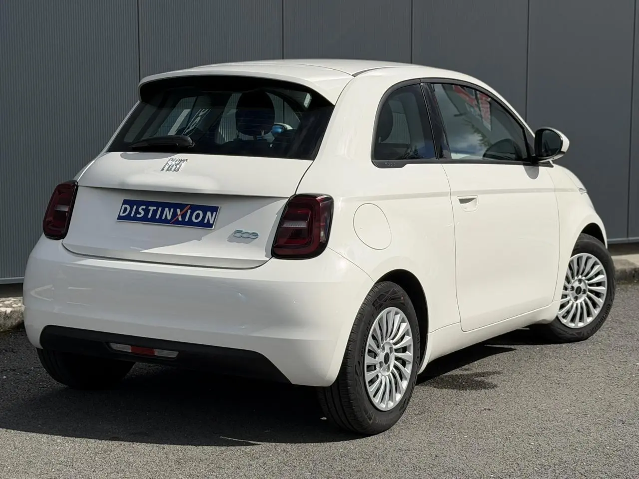 Vue 3/4 arrière droite d'une Fiat 500 électrique blanc Artic avec feux arrière foncés et jantes multibranches.